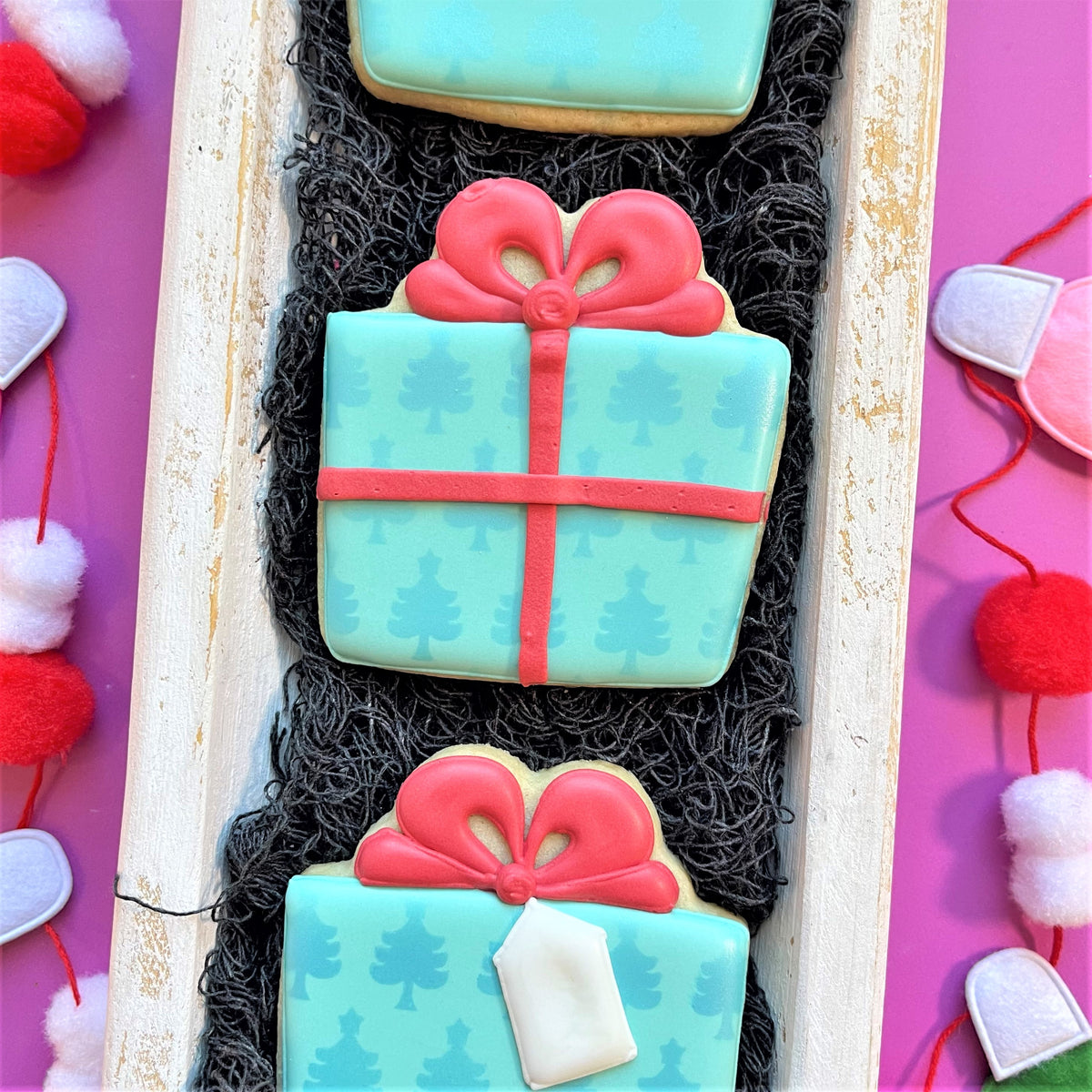 Turquoise gift box-shaped cookies with red icing bows and tree patterns made using classic present cookie cutter
