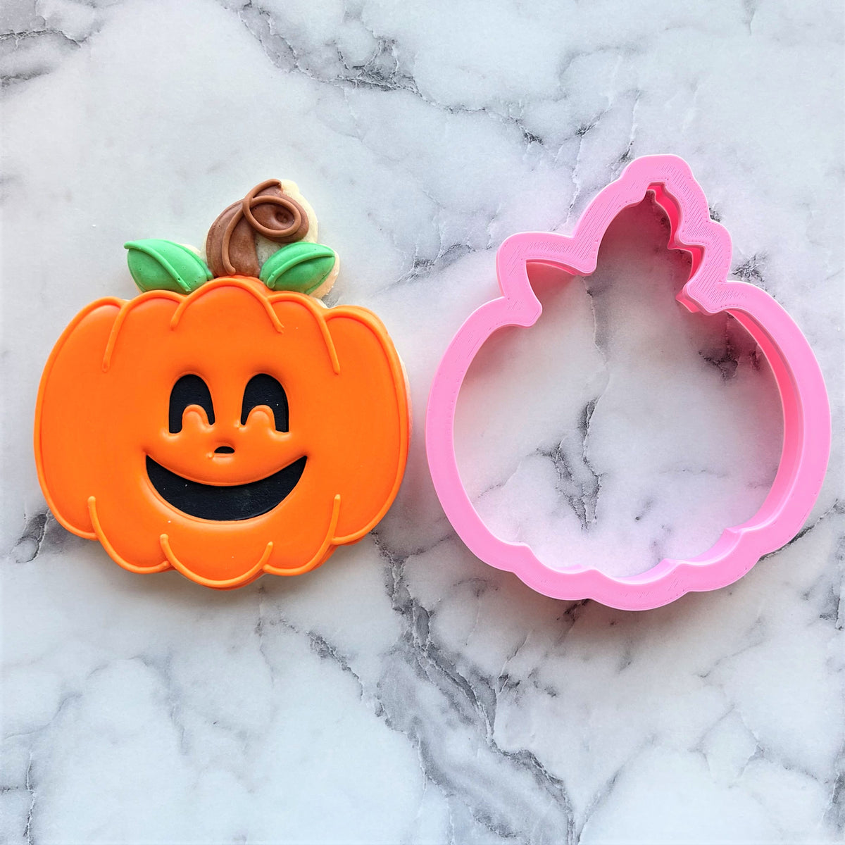 Classic pumpkin cookie cutter in orange shaped like a pumpkin with a smiling face green leaves and brown stem