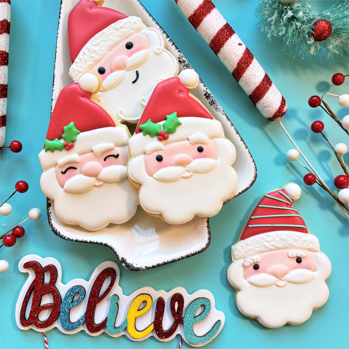 Delicate white frosted santa claus cookies with red hats and green holly accents made using classic santa cookie cutter