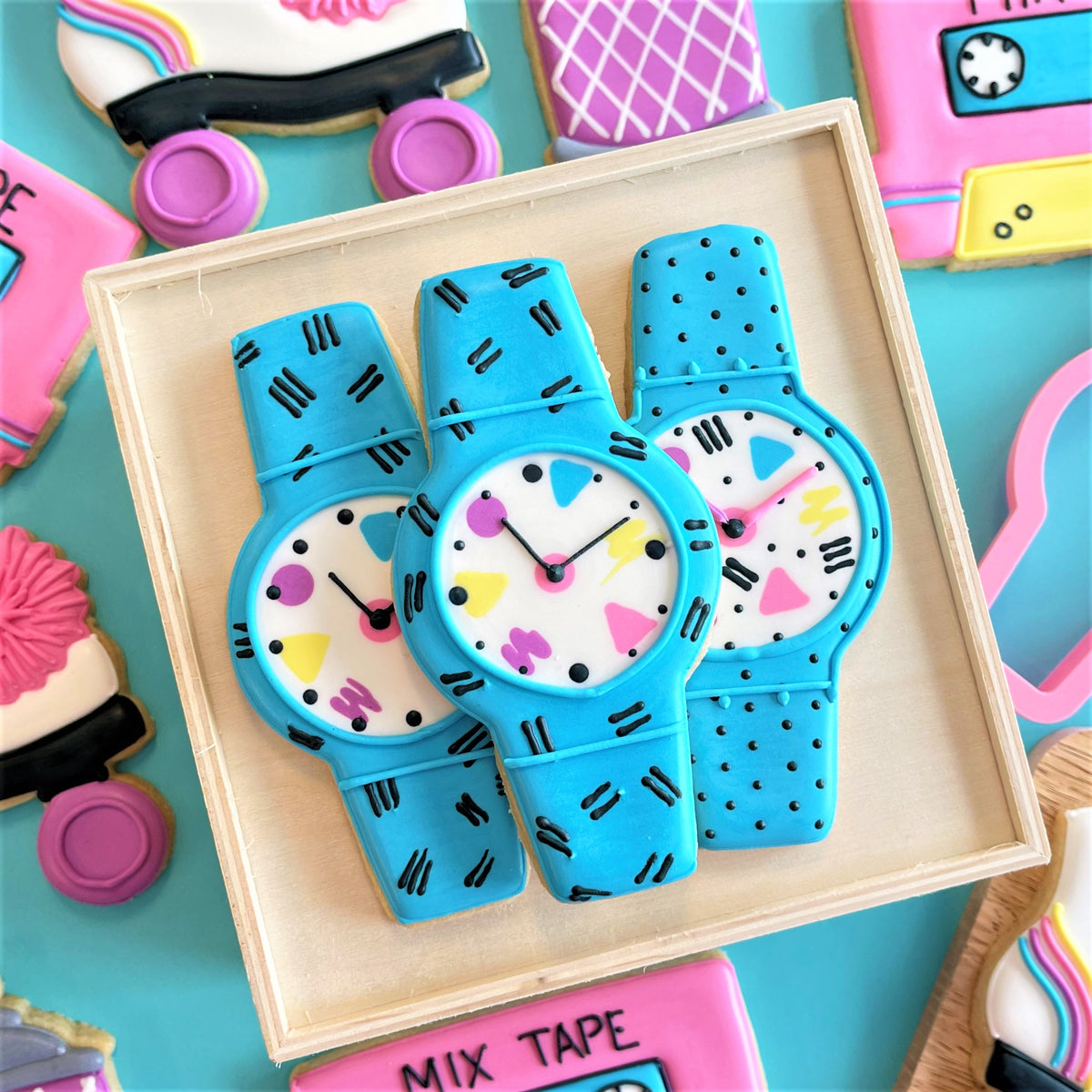 Three blue sugar cookies shaped like vintage watches with white faces and colorful geometric patterns made using cool watch cookie cutter