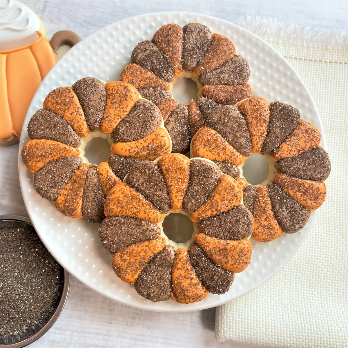 Delicate pumpkin spice cookies with alternating orange and brown chocolate-dipped sections dusted with sparkling sugar