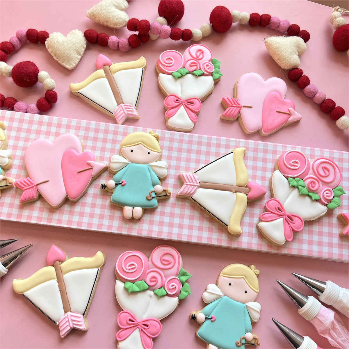 Pink and white frosted sugar cookies shaped like hearts arrows roses and a small angel figure using cupid cookie cutter