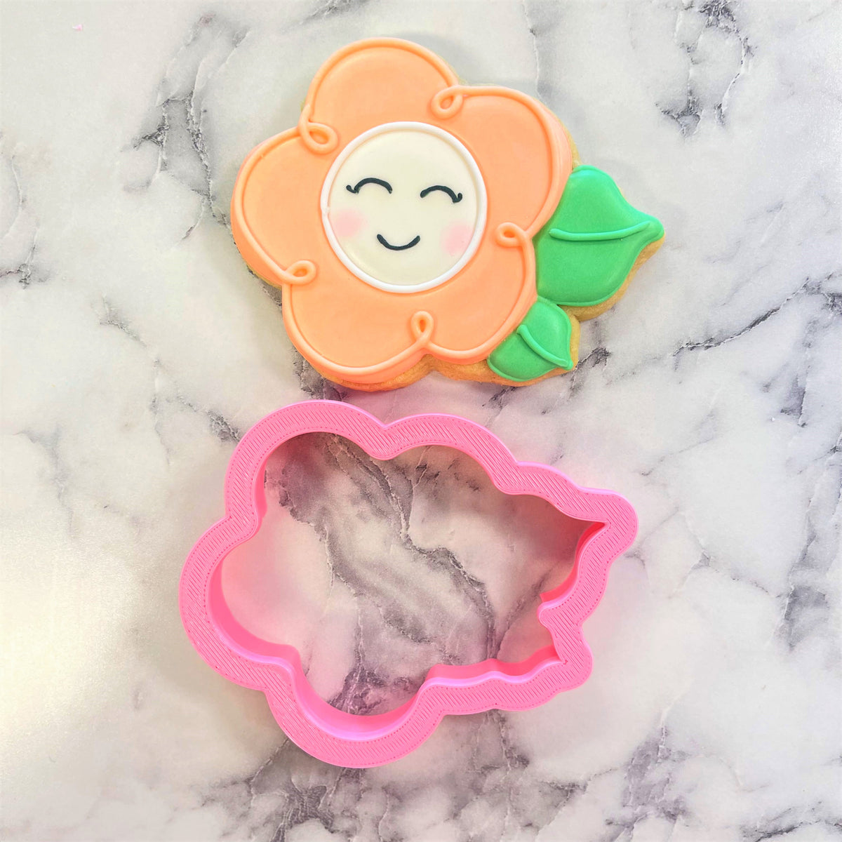 A cheerful orange flower-shaped cookie with smiling face, green leaves, and pink icing made using daisy with leaves cookie cutter