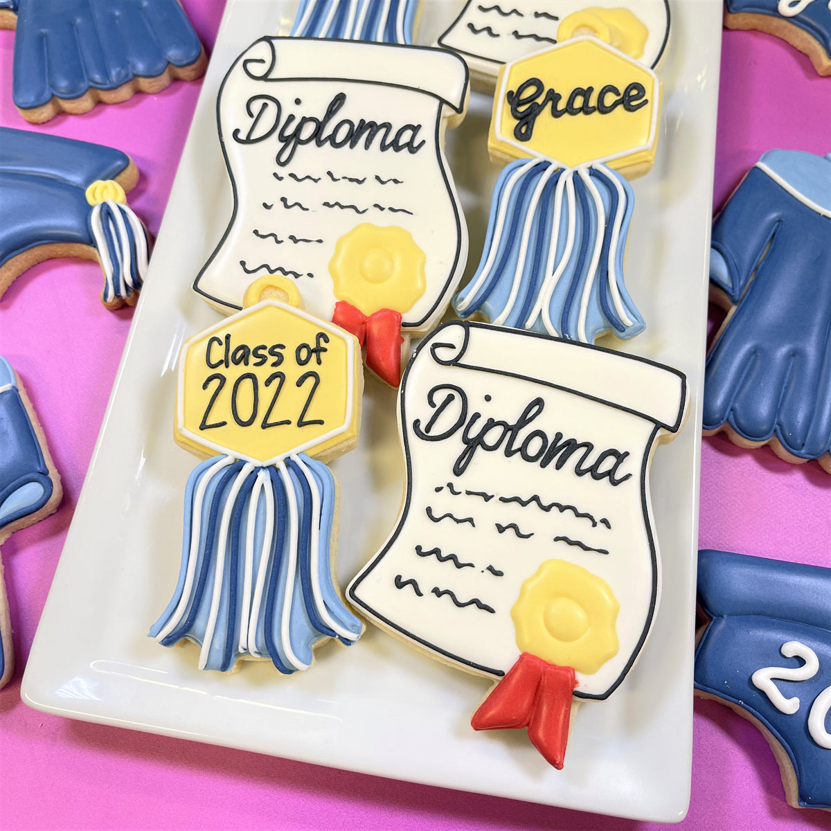 Blue and white frosted graduation diploma cookies with yellow seals and red ribbons made using graduation cookie cutter set