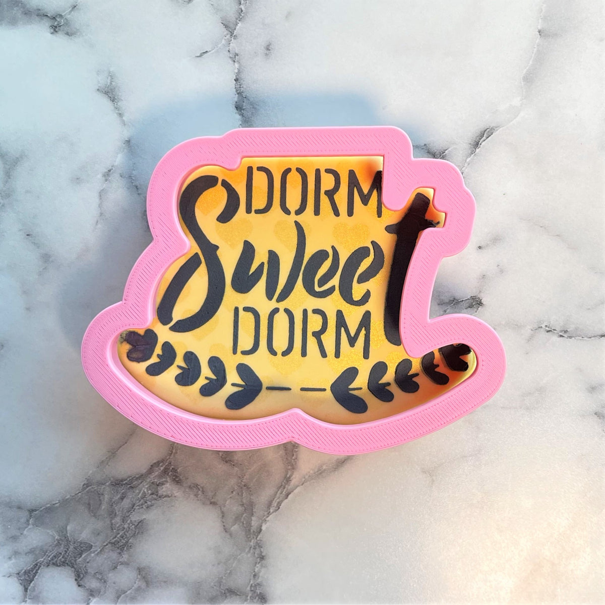Pink 3d printed cookie cutter shaped like a bed with sweet dorm text on yellow background for dorm sweet dorm plaque