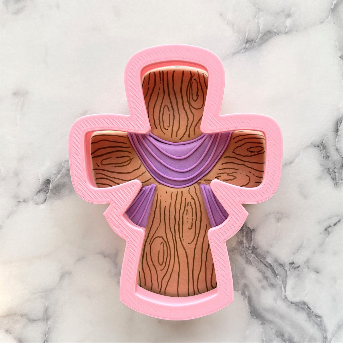 Pink cross-shaped easter cross cookie cutter with wood grain design and purple draped fabric detail
