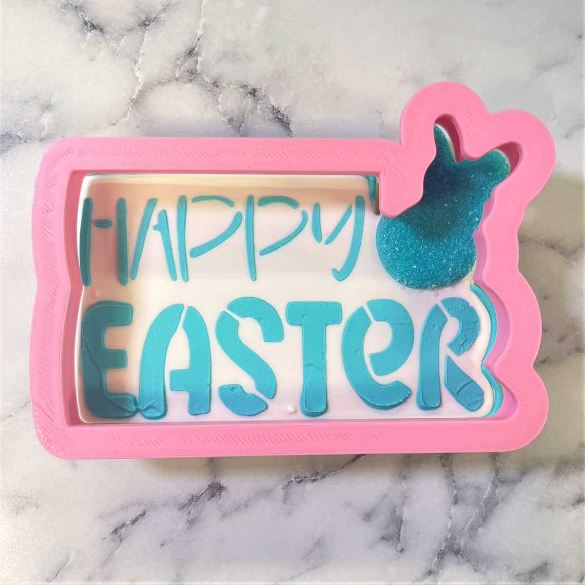 Pink rectangular silicone happy easter plaque cookie cutter with teal lettering and glittery blue bunny silhouette stencil