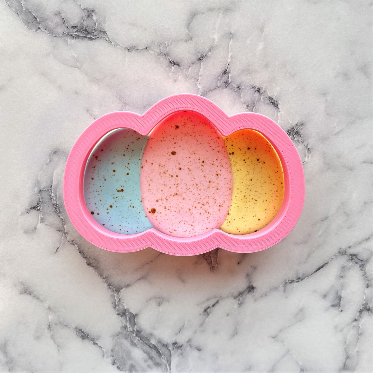 Egg cluster cookie cutter pink cloud-shaped silicone mold with three colorful speckled compartments in blue pink and yellow