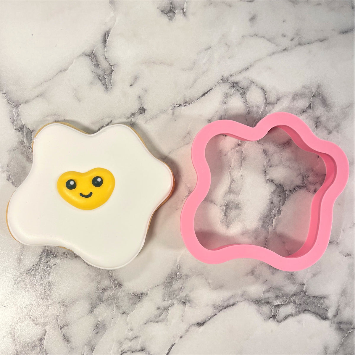 A pink silicone fried egg cookie cutter featuring a smiling yellow yolk for fun baking shapes
