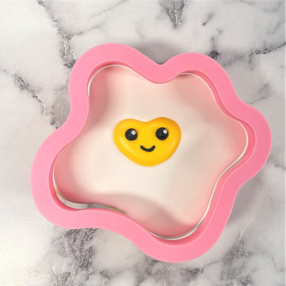 Pink silicone fried egg cookie cutter with yellow smiling yolk design for baking and shaping cookies