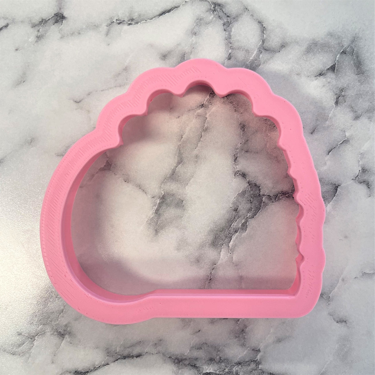 Empty tomb cookie cutter pink silicone shell-shaped mold with scalloped edge and clear interior showing marbled stone