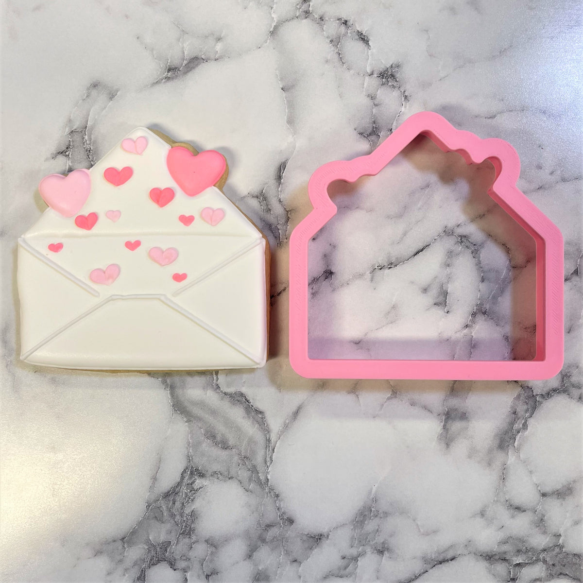 A pink silicone envelope with hearts cookie cutter next to a sugar cookie decorated with pink heart icing
