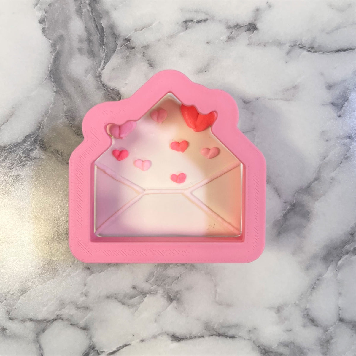 Pink silicone mini envelope cookie cutter with clear window and red heart decorations inside for baking