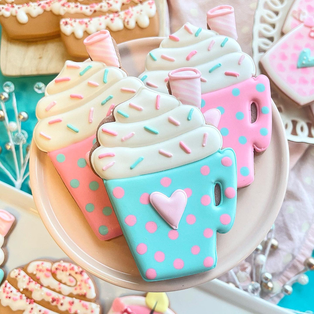 Pastel-colored sugar cookies shaped like coffee cups with white icing swirls and colorful sprinkles using latte cup with whipped cream cookie cutter