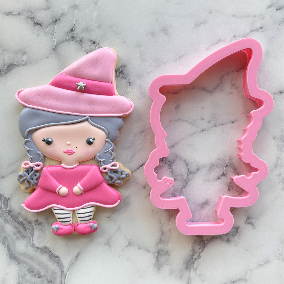 Pink plastic witch cookie cutter next to decorated sugar cookie shaped like the fab-boo-lous witch design