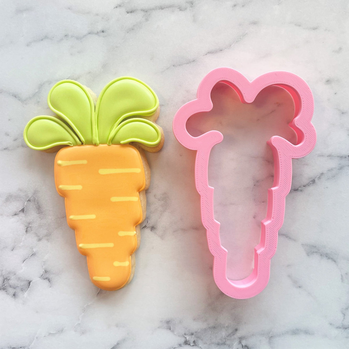 A vibrant orange carrot-shaped cookie made using a pink plastic floppy carrot cookie cutter with green leafy top