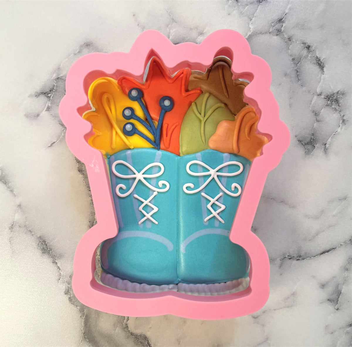 Pink silicone flower boots cookie cutter shaped like blue lace-up boots filled with colorful flowers