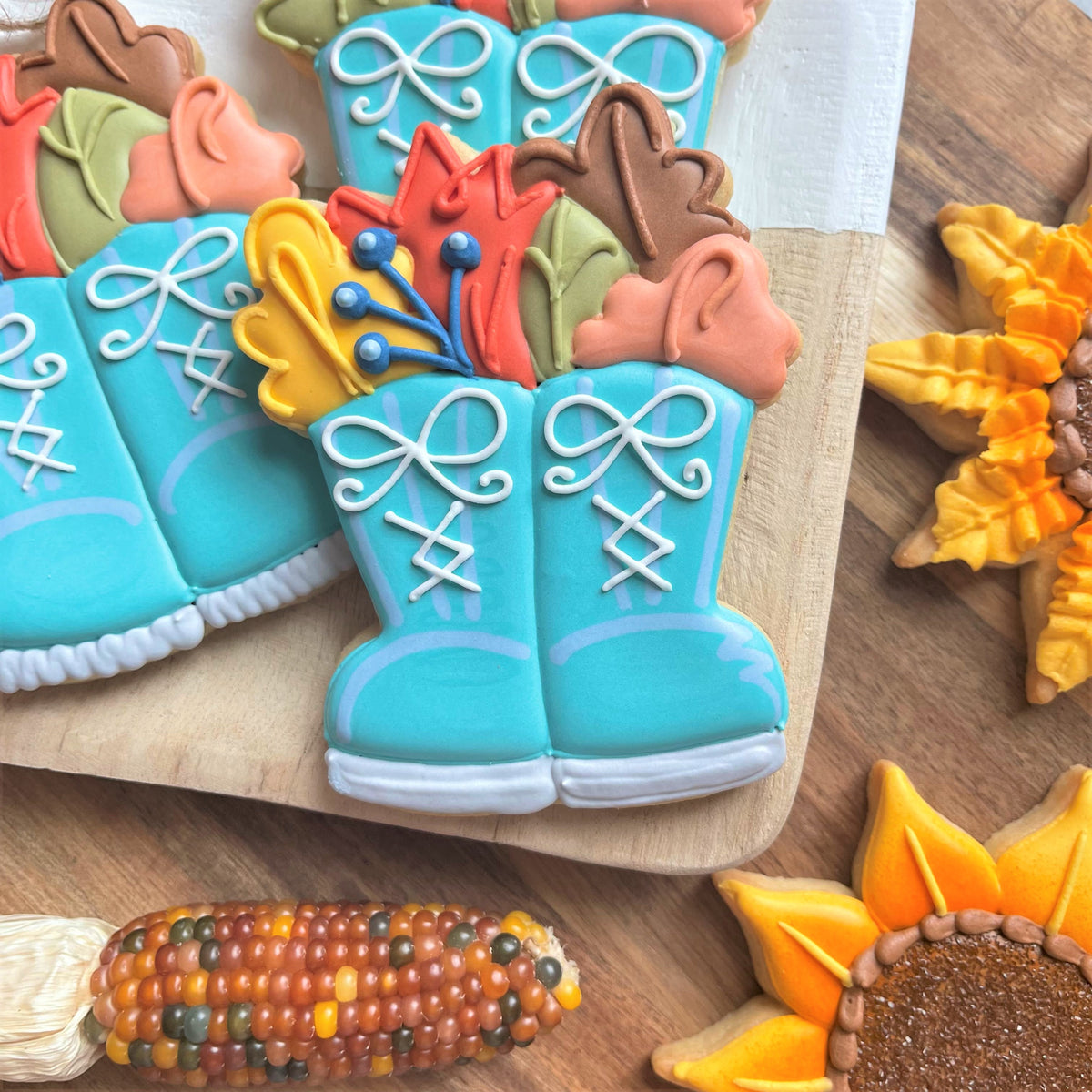 Turquoise boot-shaped sugar cookies with white icing laces and bows filled with colorful autumn leaves using flower boots cookie cutter