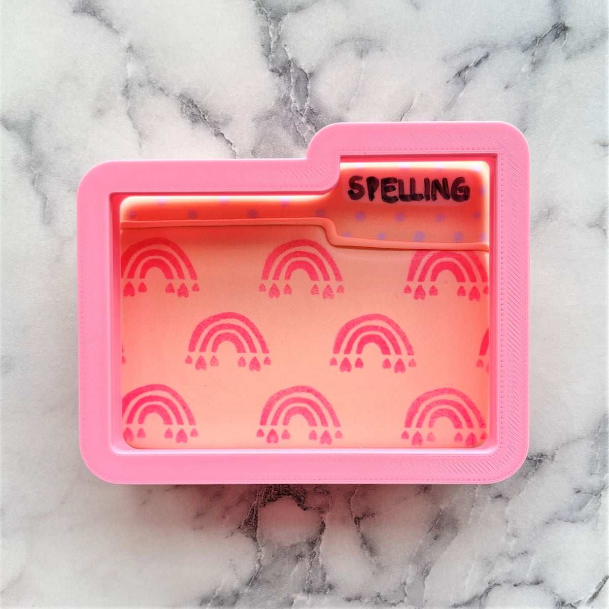 Pink silicone folder cookie cutter organizer with translucent orange interior rainbow patterns and spelling tab label