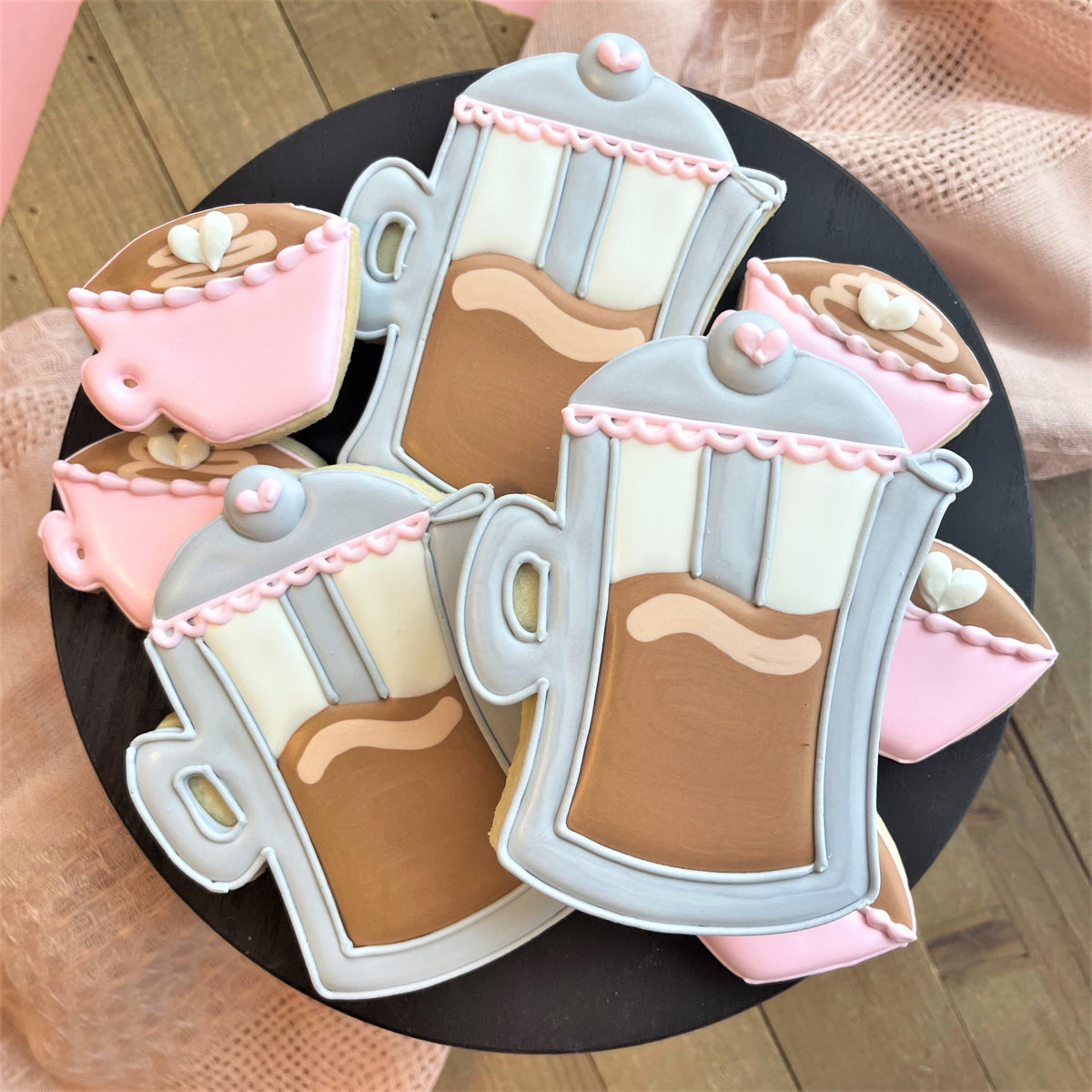 Delicate pink and gray sugar cookies shaped like coffee mugs with brown icing swirls and heart decorations from french press with mini coffee cup cookie cutter set