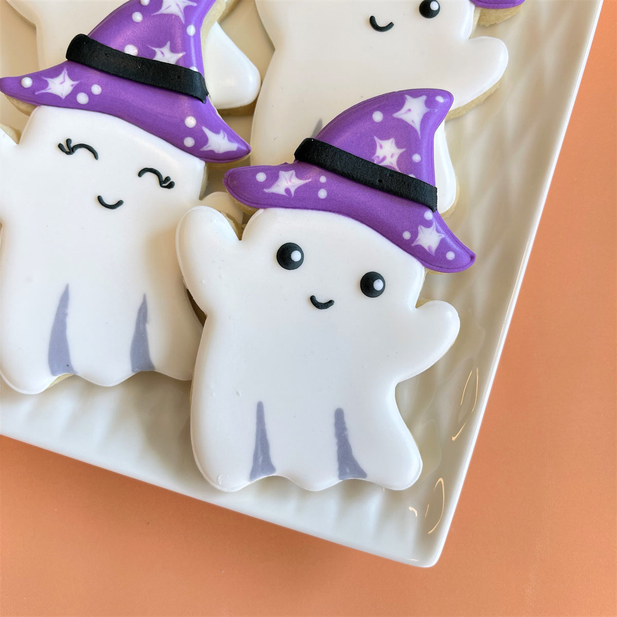 White ghost-shaped cookies with purple witch hats decorated with white stars from haunted house cookie class recording