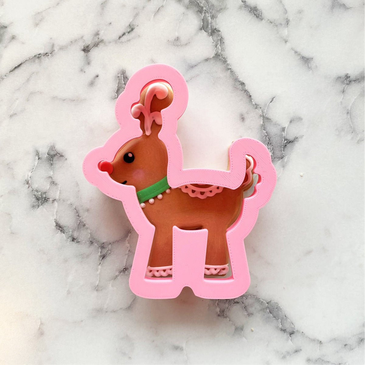 Pink plastic gingerbread reindeer cookie cutter with brown interior green collar and red nose for festive baking