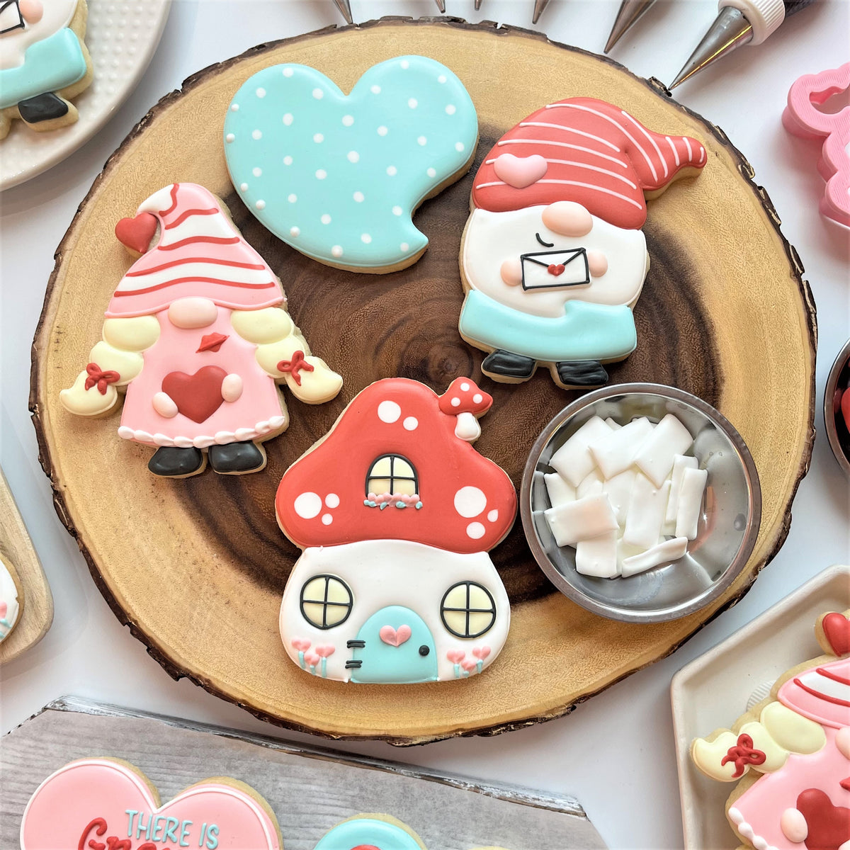 Pastel-colored sugar cookies shaped like gnomes mushroom house and hearts with delicate icing from gnome online cookie decorating class recording
