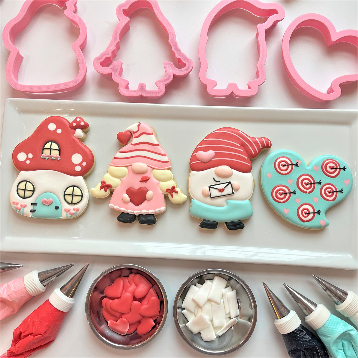 Pink plastic cookie cutters shaped like a mushroom house gnomes and hearts for gnome online cookie decorating class recording