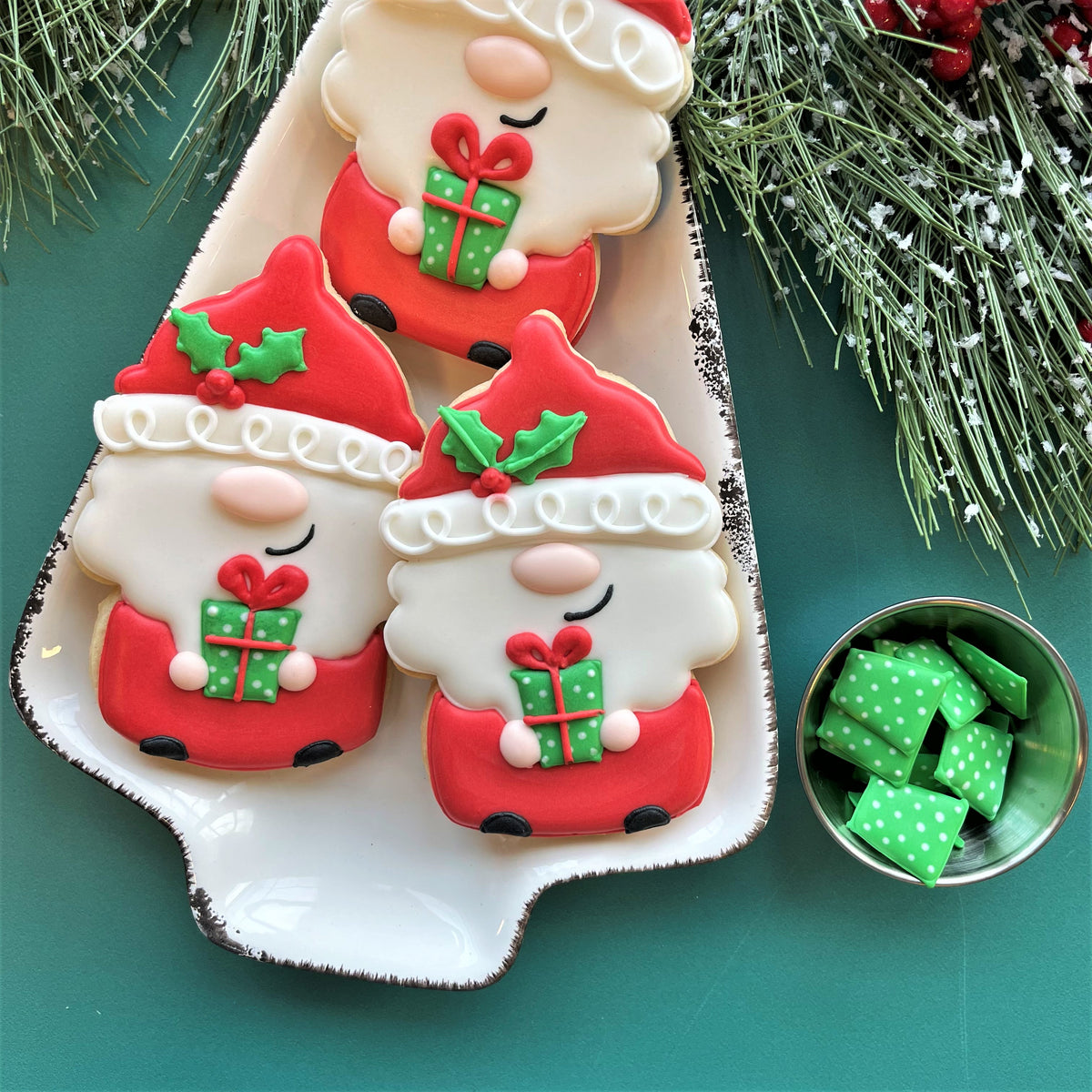 Three festive red and white santa claus cookies holding green polka dot gifts made with uncle sam gnome cookie cutter