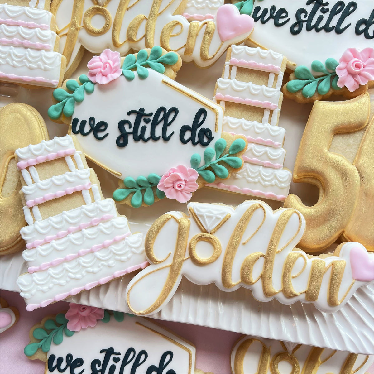 Delicate white and gold floral plaque cookie with we still do script pink sugar flowers and mint green leaves for weddings
