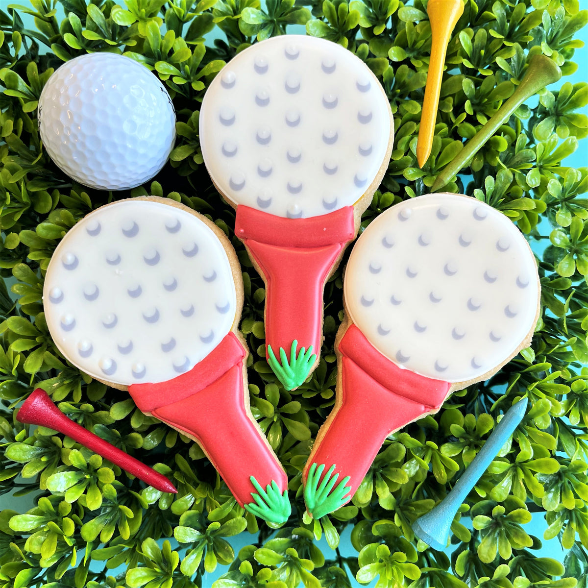 Three golf club-shaped cookies with white dotted heads and red handles decorated with green icing from golf cookie decorating class recording
