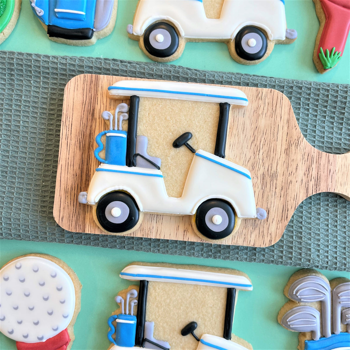 A white and blue decorated golf cart cookie with black wheels and a blue bag of clubs for a golf cookie class recording