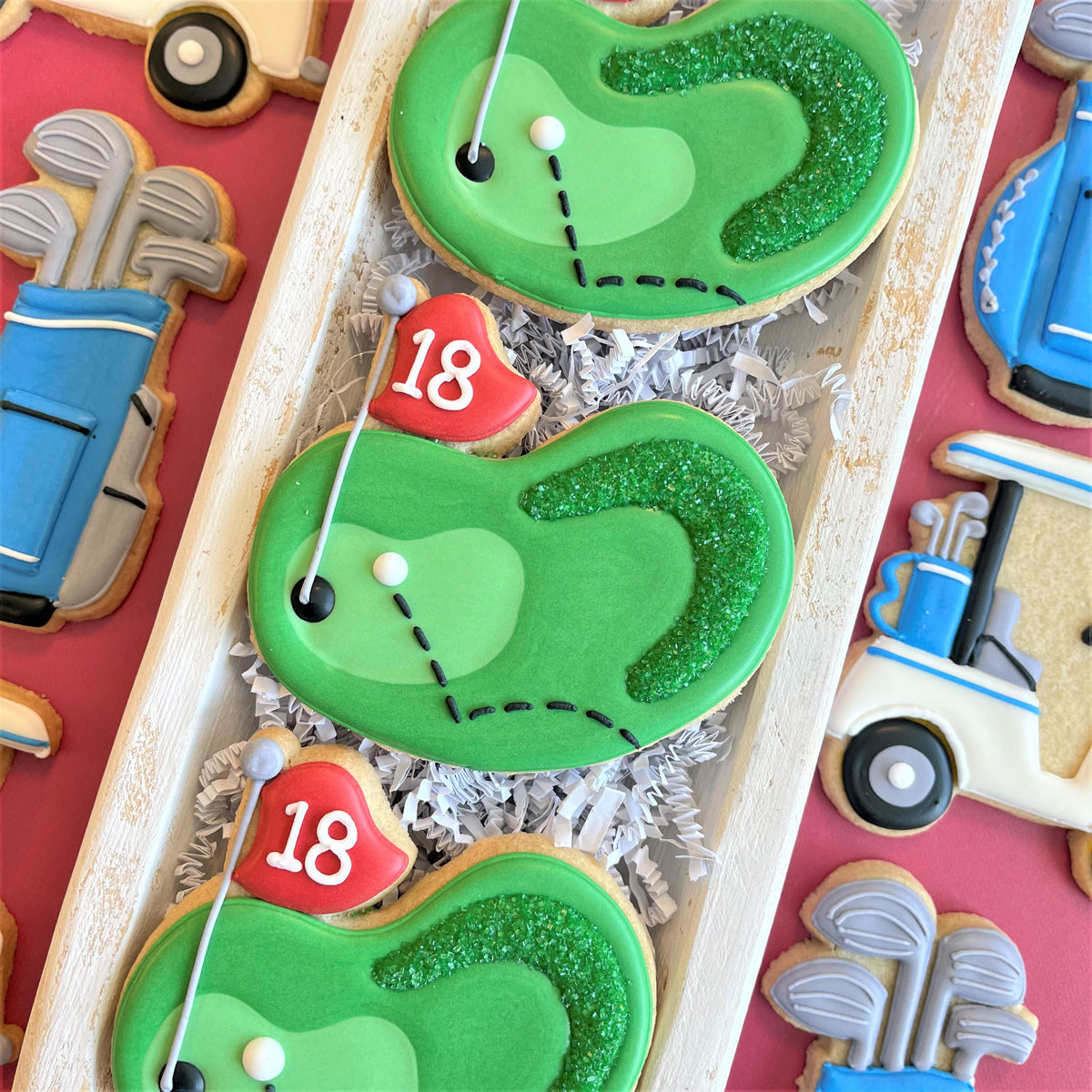 Green glittery golf course cookies with white icing details and red flag markers in golf cookie decorating class recording