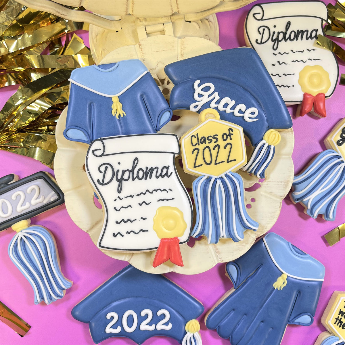 Blue graduation-themed sugar cookies shaped with diploma with seal cookie cutter featuring white icing details