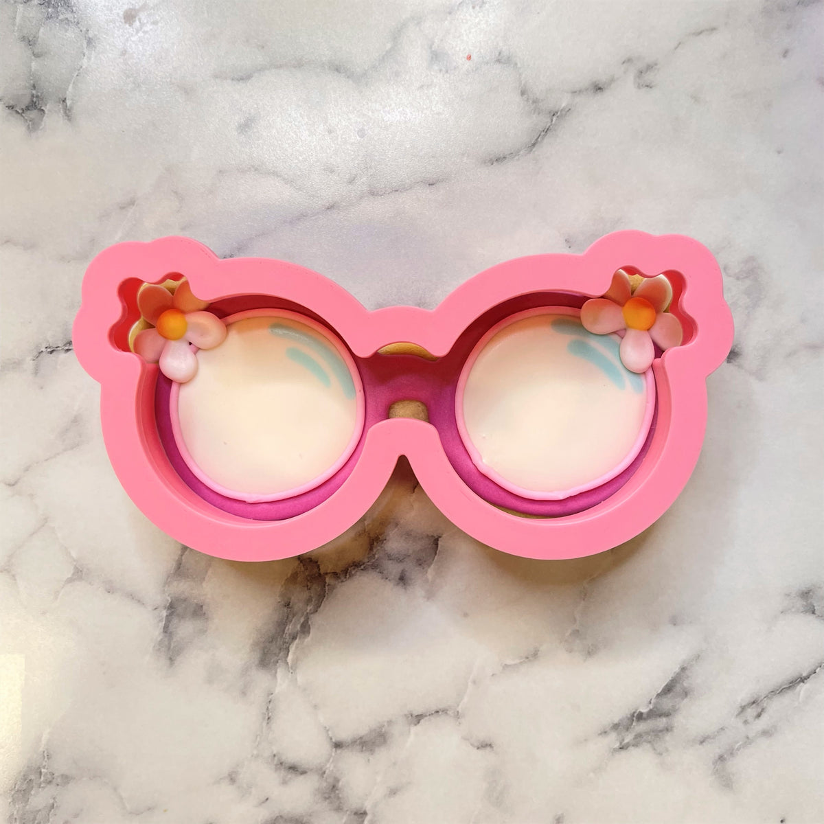 Pink silicone groovy sunglasses cookie cutter shaped like oversized glasses with small flower decorations on temples
