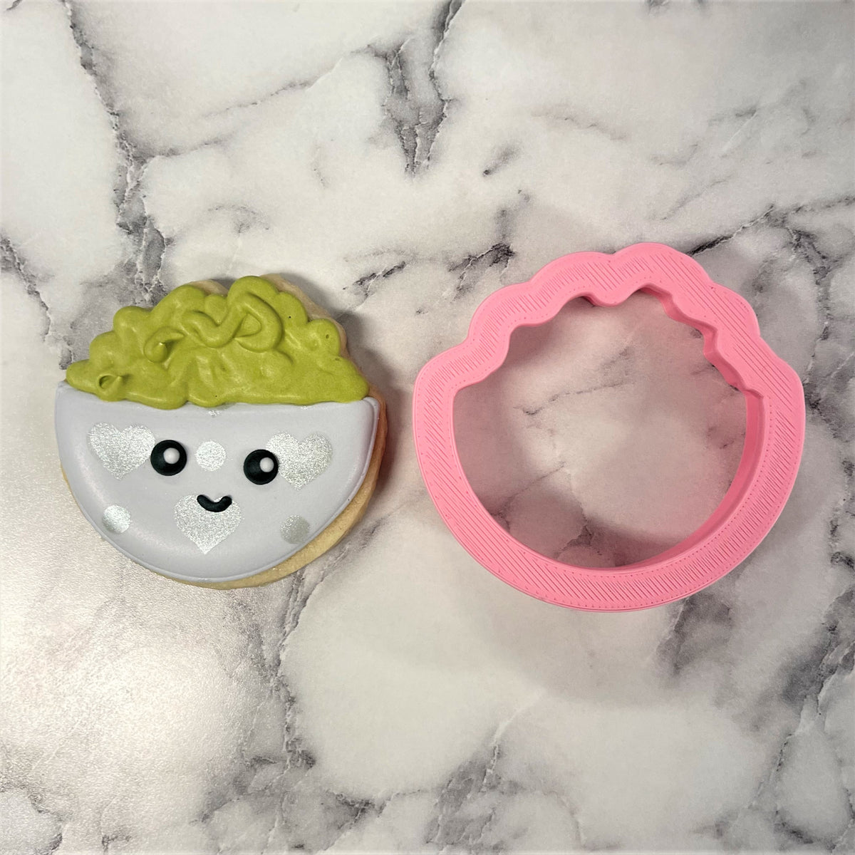 A pink scalloped-edged mini guacamole cookie cutter with smooth plastic finish beside a decorated brain cookie