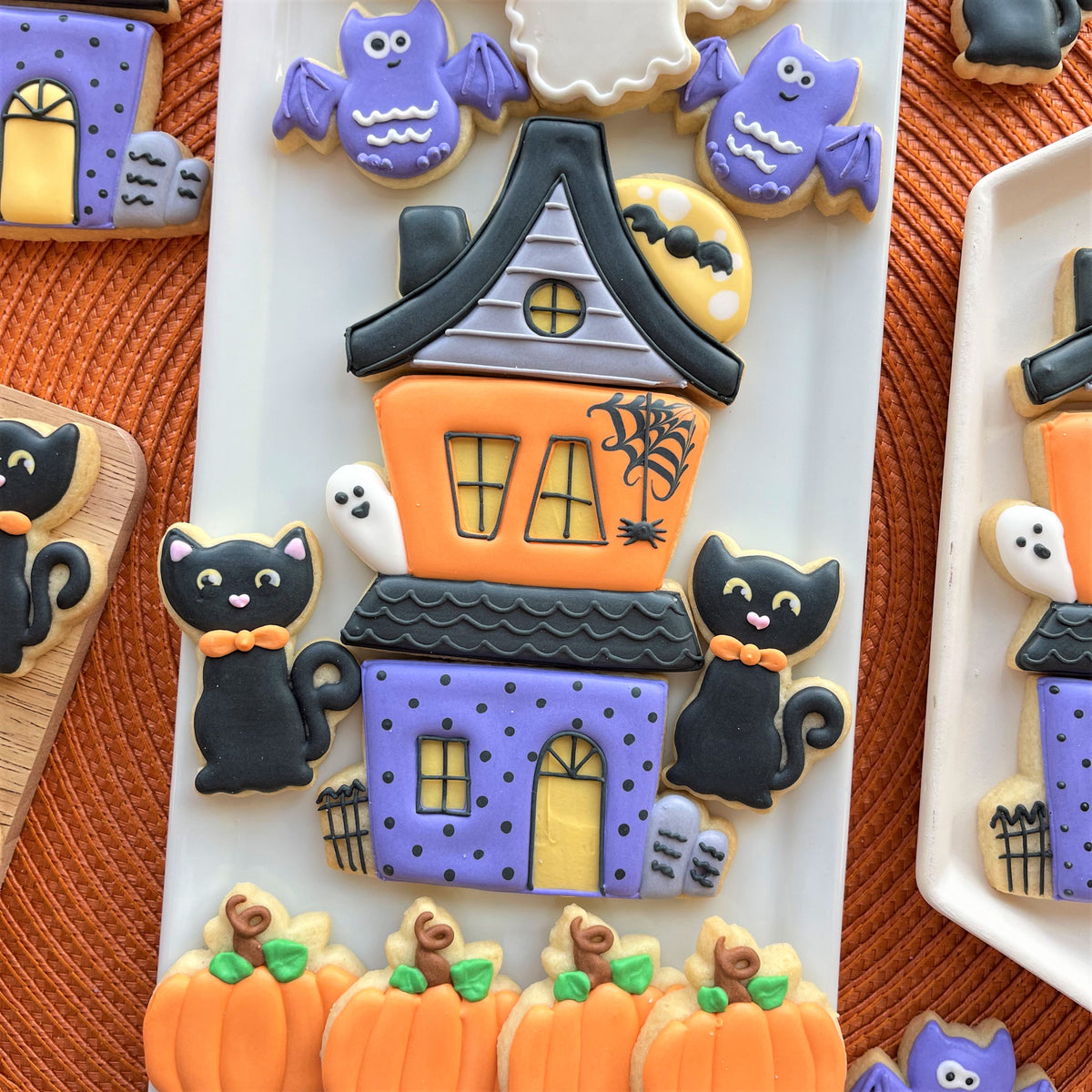 A halloween-themed sugar cookie shaped like a haunted house with orange purple and black icing from haunted house 3-in-1 cutter bundle