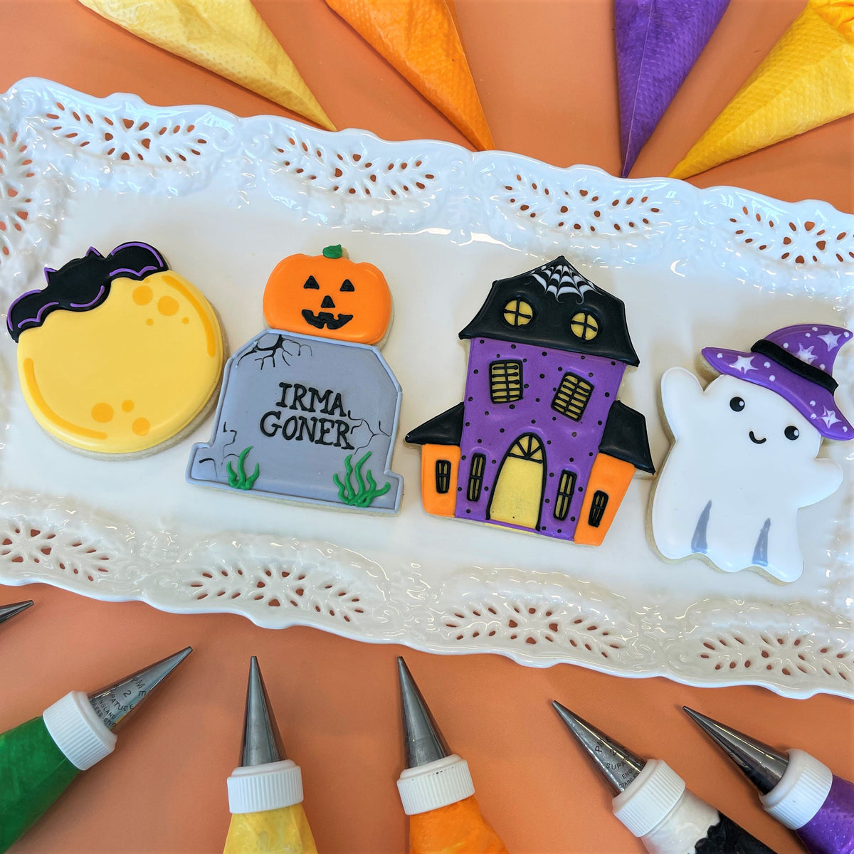 Halloween-themed sugar cookies shaped like yellow moon with bat wings, pumpkin tombstone, haunted house, and ghost for haunted house online cookie decorating class recording