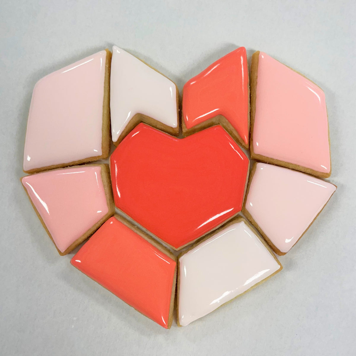 Heart puzzle cookie cutter featuring a glossy heart-shaped cookie with vibrant coral center and pink white icing pieces