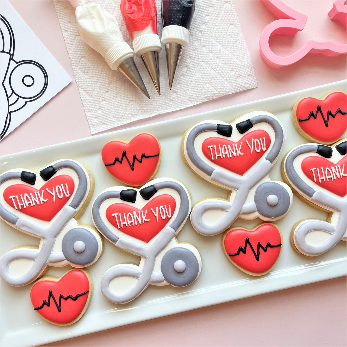 Red and gray stethoscope-shaped sugar cookies with thank you in white icing made using stethoscope heart cookie cutter