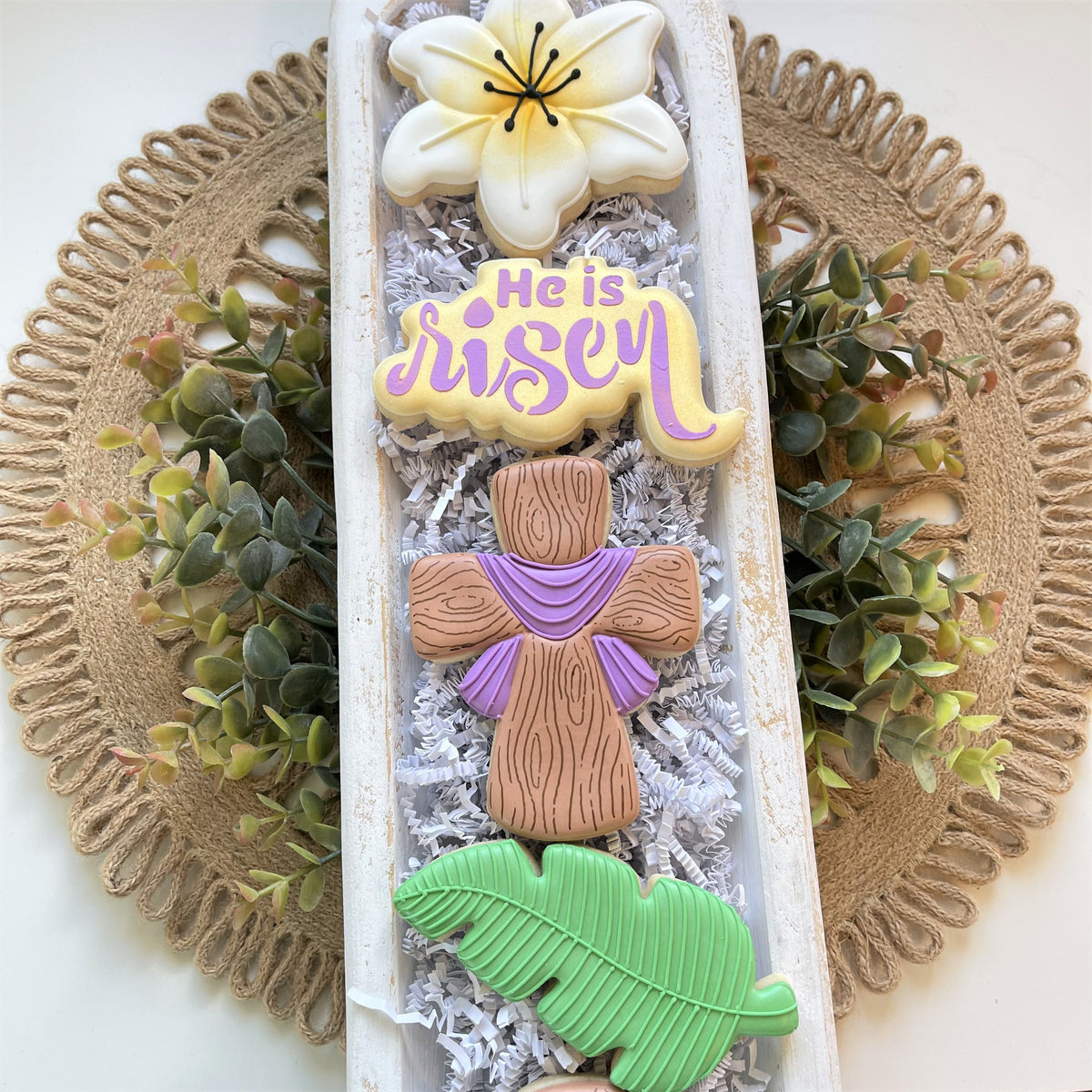 A decorative white wooden tray holding intricately designed flower and cross shaped cookies made with lily cookie cutter