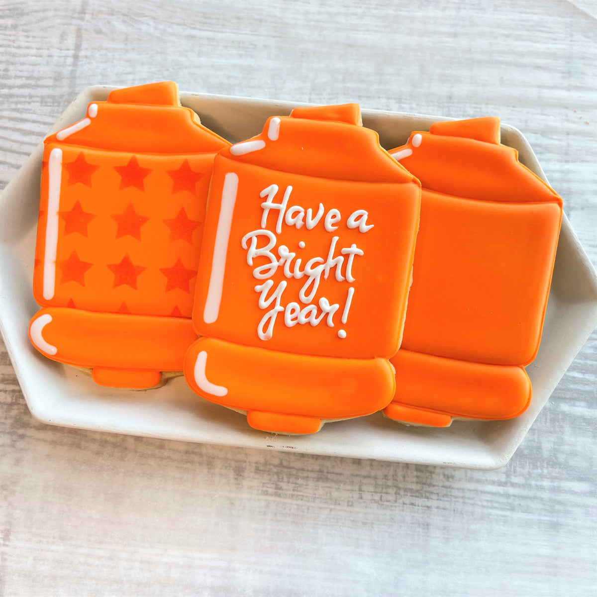 Orange sugar cookies shaped like lanterns decorated with white icing stars and have a bright year message using chubby xl highlighter cookie cutter
