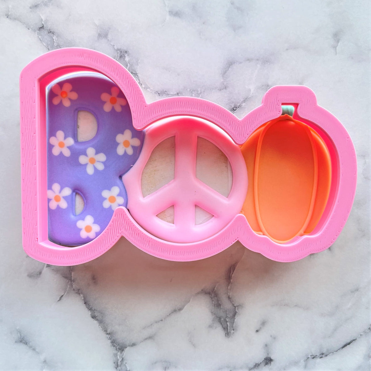 Pink plastic boo cookie cutter with purple floral interior peace sign center and orange pumpkin detail for halloween
