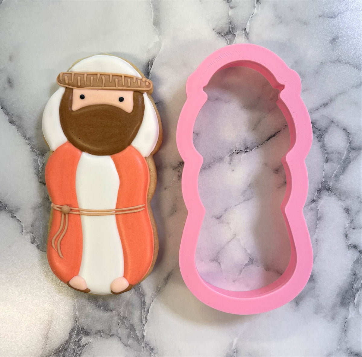 A pink silicone joseph cookie cutter next to an intricately decorated sugar cookie with matching design