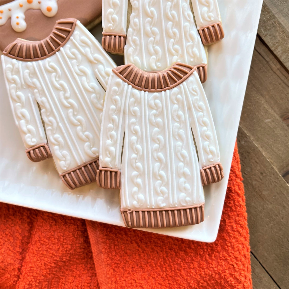 White and beige sugar cookies shaped like cable knit sweaters with detailed textured patterns for fall decorating class recording