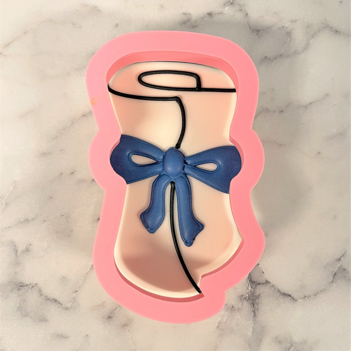 Pink silicone grad diploma rolled cookie cutter shaped like a graduation cap with blue ribbon and black outline details