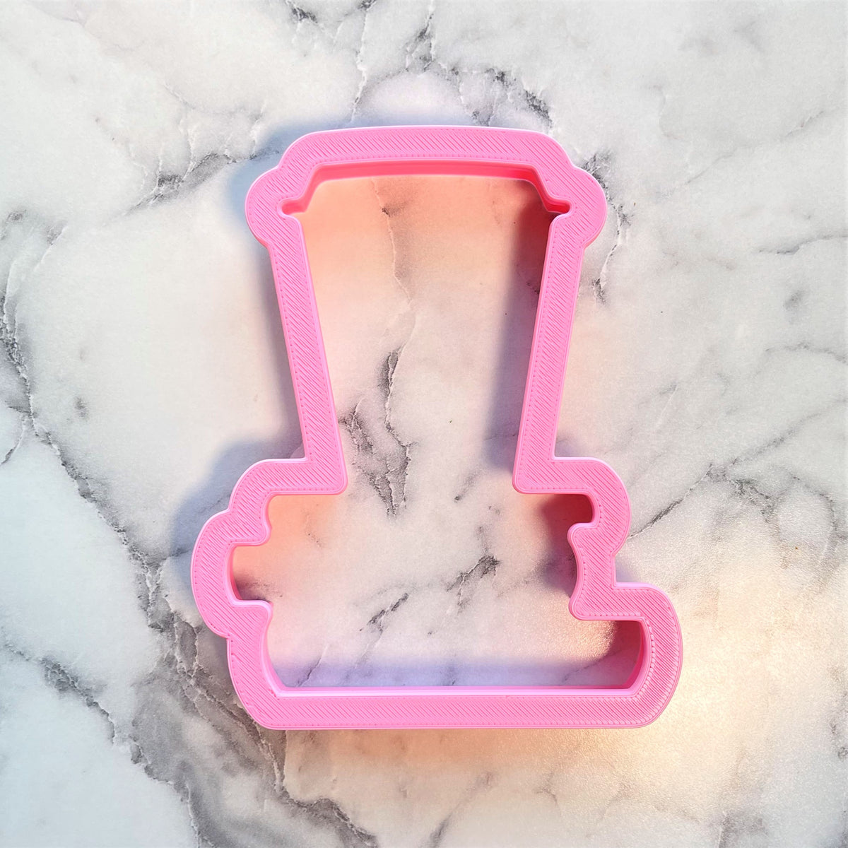Pink plastic cookie cutter shaped like a top hat from latte on books for baking and decorating cookies