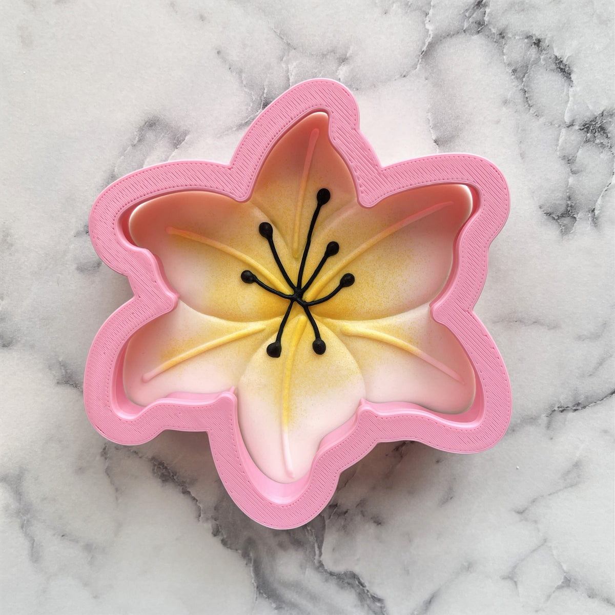 Pink silicone lily cookie cutter with gradient yellow to pink interior and black stamen details for flower shaped cookies