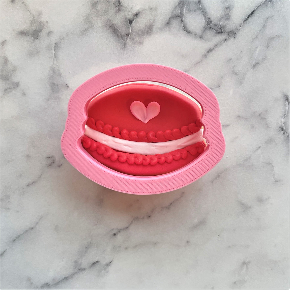 Pink silicone mini macaron cookie cutter mold with red and white interior details and a small heart design