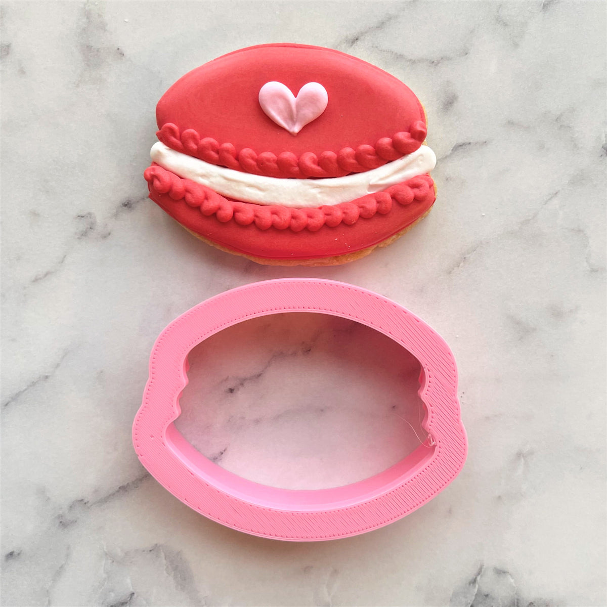 Mini macaron cookie cutter in pink with a glossy finish and detailed ridged edges for baking use